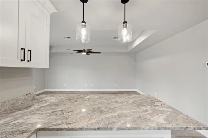 Kitchen featuring white cabinets, pendant lighting, light stone counters, ceiling fan, and a tray ceiling