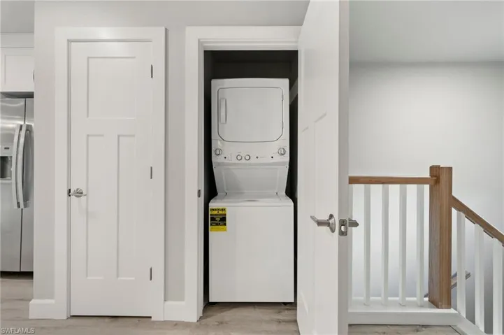 Laundry room with stacked washer and clothes dryer and light hardwood / wood-style flooring