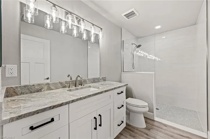 Bathroom with wood-style floors, toilet, vanity, and a tile shower