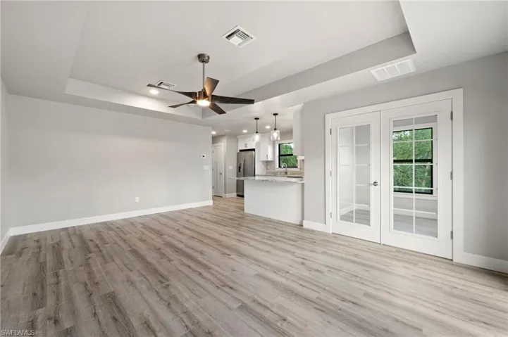 Unfurnished living room featuring light hardwood / wood-style floors, ceiling fan, and a raised ceiling