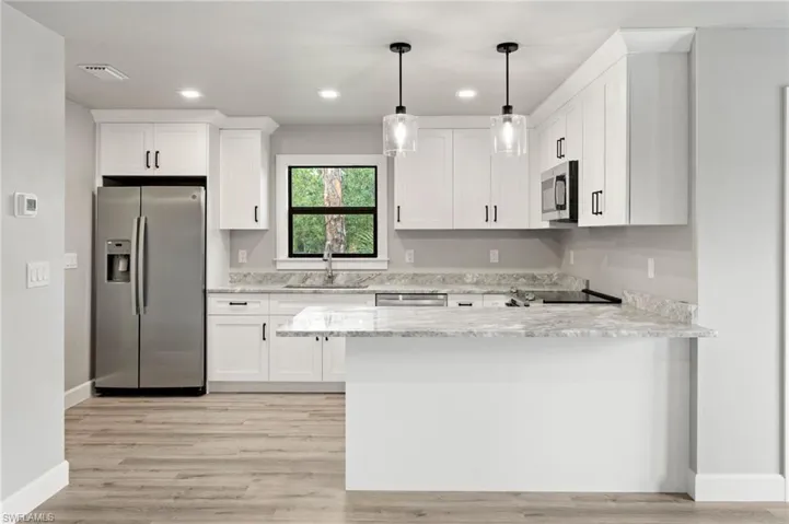 Kitchen with appliances with stainless steel finishes, white cabinets, sink, kitchen peninsula, and light wood-type flooring