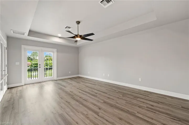 Unfurnished room with wood-style floors, french doors, a raised ceiling, and ceiling fan