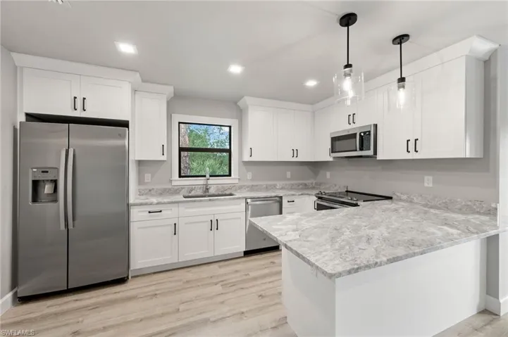 Kitchen featuring stainless steel appliances, sink, light hardwood / wood-style floors, decorative light fixtures, and white cabinetry