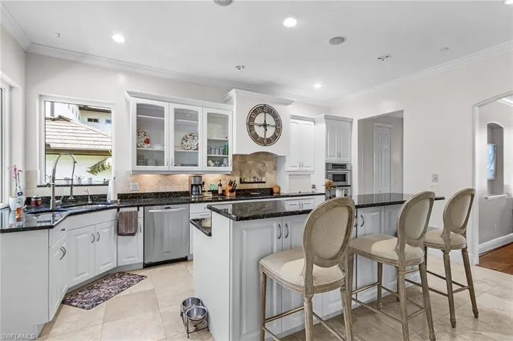 Kitchen with white cabinetry, ornamental molding, dark stone counters, glass insert cabinets, and healthy amount of natural light