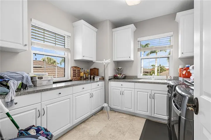 Kitchen with white cabinets, washer and clothes dryer, stove, light tile patterned floors, and dark stone countertops