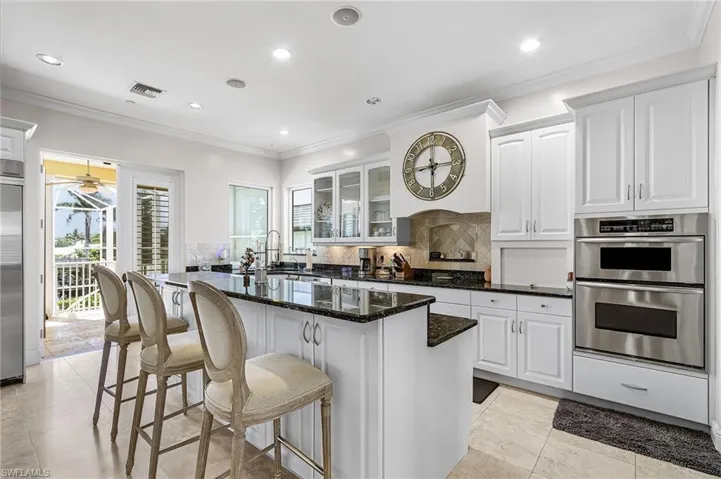 Kitchen with crown molding, white cabinets, glass insert cabinets, dark stone counters, and a breakfast bar area