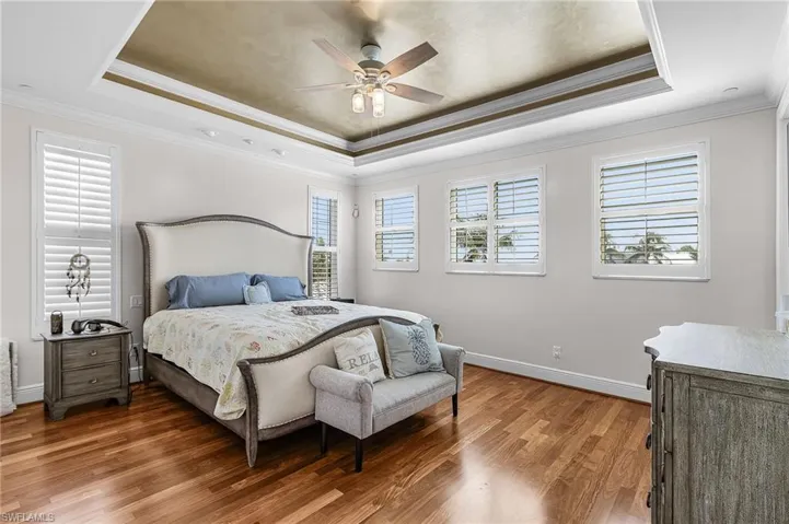 Bedroom with a tray ceiling, crown molding, light wood finished floors, and ceiling fan
