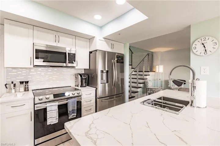 Kitchen with light stone counters, stainless steel appliances, white cabinetry, and sink