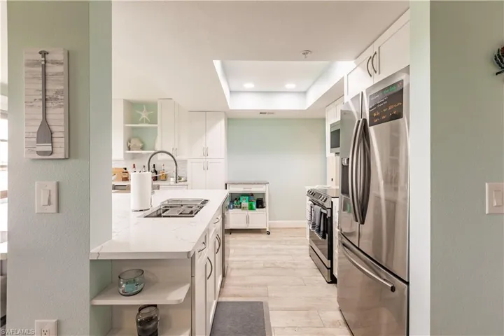 Kitchen featuring white cabinets, light hardwood / wood-style flooring, stainless steel appliances, sink, and a tray ceiling