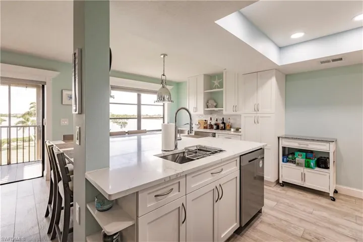Kitchen with dishwasher, a healthy amount of sunlight, light wood-type flooring, light stone counters, and pendant lighting