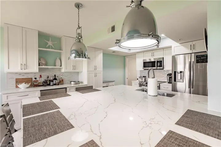 Kitchen with tasteful backsplash, stainless steel appliances, light stone counters, hanging light fixtures, and white cabinets