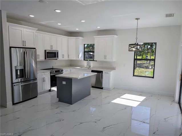 Kitchen with a kitchen island, white cabinetry, hanging light fixtures, and appliances with stainless steel finishes