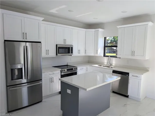 Kitchen featuring white cabinets, sink, appliances with stainless steel finishes, a kitchen island, and light stone counters