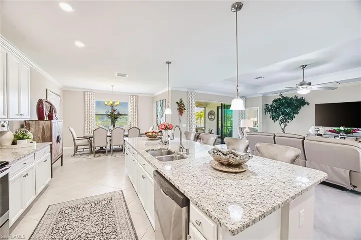 Kitchen featuring white cabinetry, light stone countertops, pendant lighting, stainless steel dishwasher, and crown molding. large island