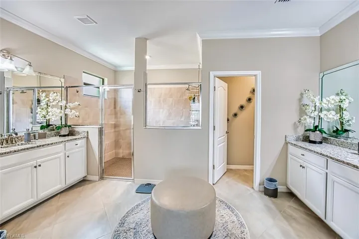 Ensuite Bathroom with two vanities, a roomy shower, light tile patterned floors, and crown molding