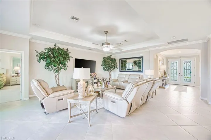Living area featuring arched walkways, french doors, a raised ceiling, a ceiling fan, and crown molding