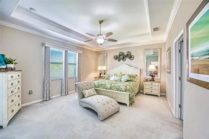 Primary Bedroom with crown molding, light colored carpet, ceiling fan, and a tray ceiling