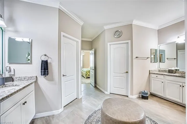 Primary Bathroom with two vanities, ornamental molding, and light tile patterned floors