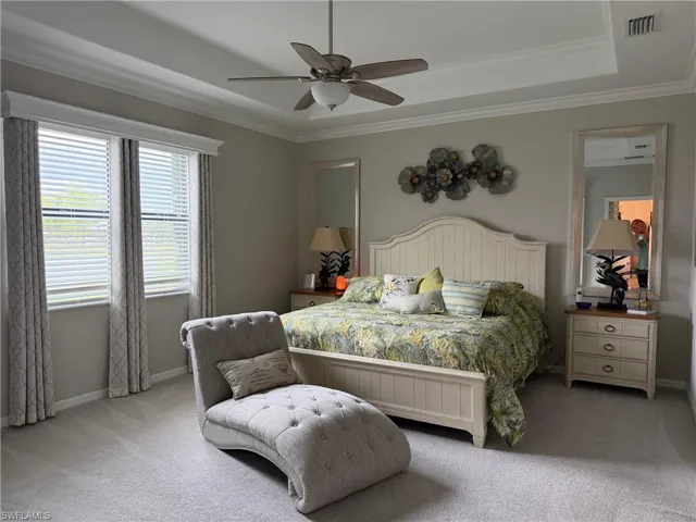 Primary Bedroom featuring carpet floors, ceiling fan, crown molding, and a tray ceiling
