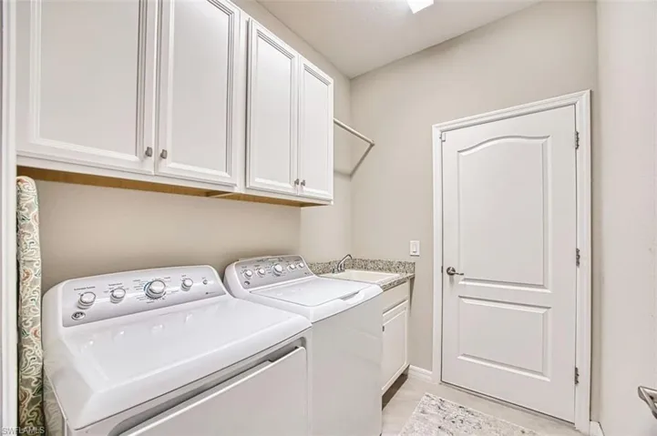 Laundry room with washing machine and dryer and cabinets and hanging clothes rack above laundry sink