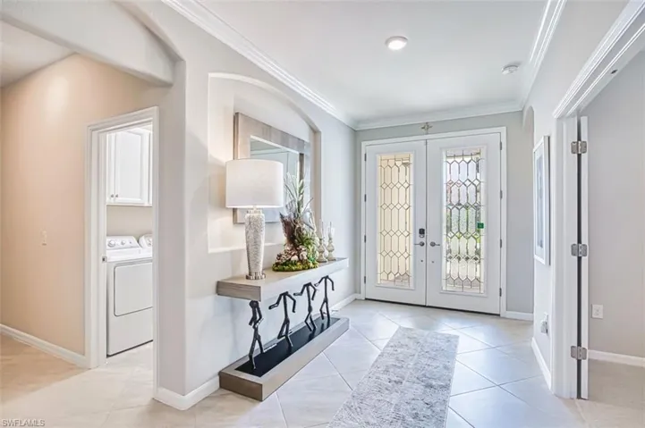 Entrance foyer with french doors, ornamental molding, light tile patterned flooring, arched walkways, and separate washer and dryer
