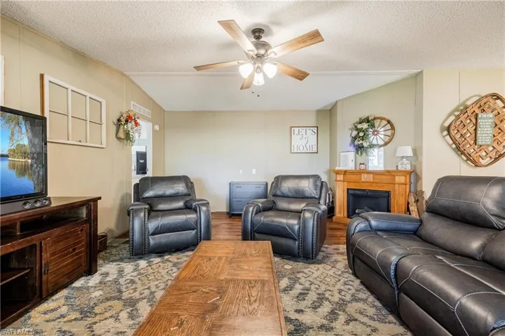 Living room with vaulted ceiling, ceiling fan, hardwood / wood-style flooring, and a textured ceiling