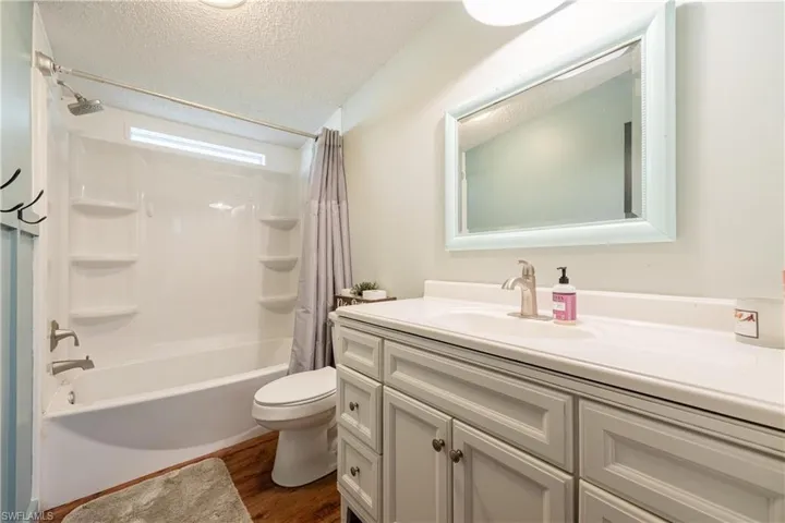 Full bathroom featuring wood-type flooring, a textured ceiling, shower / tub combo with curtain, vanity, and toilet