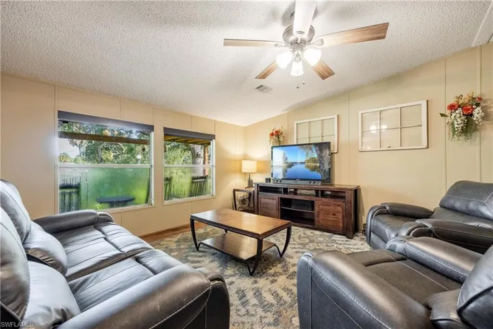 Living room with a textured ceiling, vaulted ceiling, and ceiling fan
