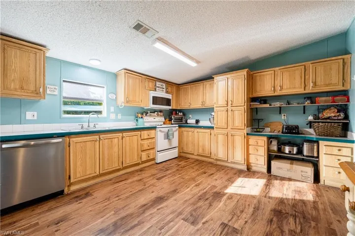 Kitchen with lofted ceiling, sink, white appliances, a textured ceiling, and light hardwood / wood-style flooring