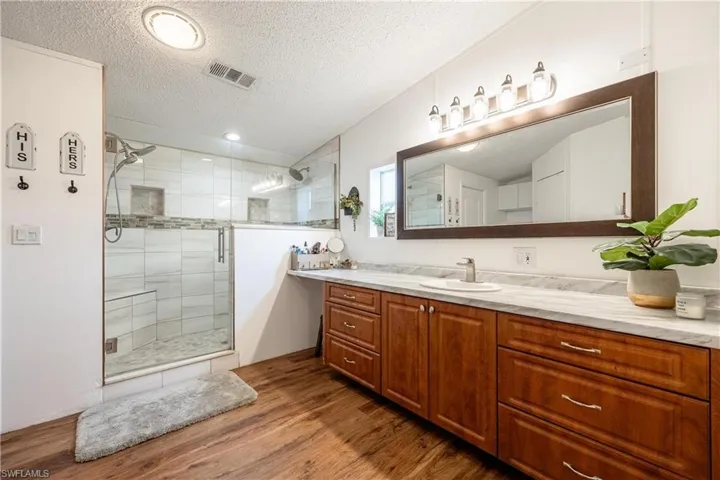Bathroom featuring vaulted ceiling, a shower with shower door, vanity, a textured ceiling, and hardwood / wood-style flooring