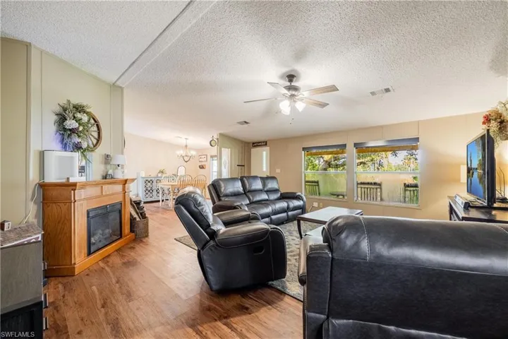 Living room featuring wood-type flooring, a textured ceiling, and ceiling fan with notable chandelier