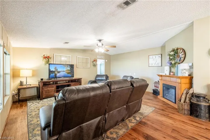 Living room featuring light hardwood / wood-style flooring, lofted ceiling, ceiling fan, and a textured ceiling