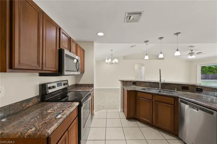 Kitchen with stainless steel appliances, lofted ceiling, a chandelier, light tile patterned flooring, and pendant lighting
