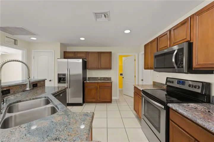 Kitchen with stainless steel appliances, light tile patterned flooring, brown cabinetry, dark stone countertops, and recessed lighting