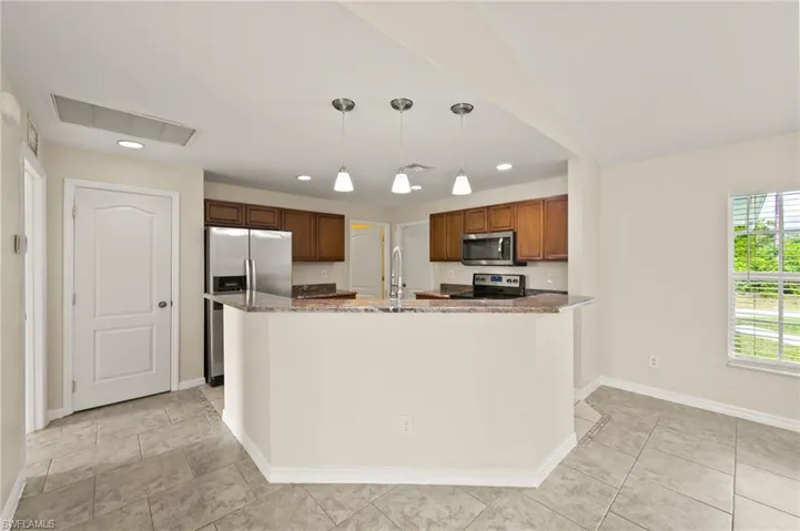 Kitchen featuring appliances with stainless steel finishes, hanging light fixtures, brown cabinets, recessed lighting, and dark stone counters