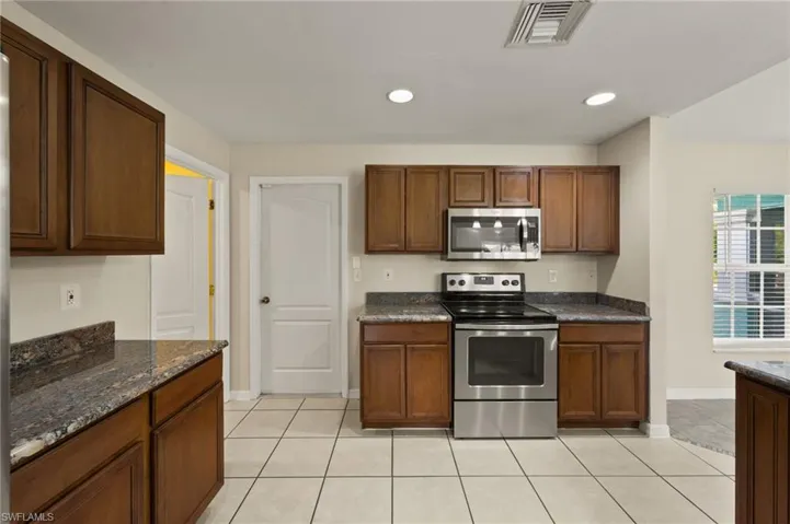 Kitchen featuring stainless steel appliances, light tile patterned floors, recessed lighting, and dark stone countertops