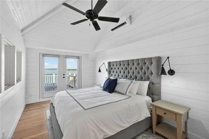 2nd floor loft Bedroom with wooden walls, wood finished floors, a water view, access to outside, and a wall mounted air conditioner