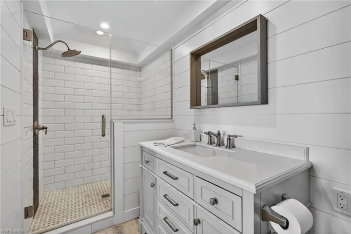 Bathroom featuring vanity, a glass shower, recessed lighting, and tile walls