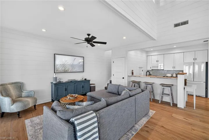 Living room with light wood-style floors, wooden walls, ceiling fan, recessed lighting, and stairs