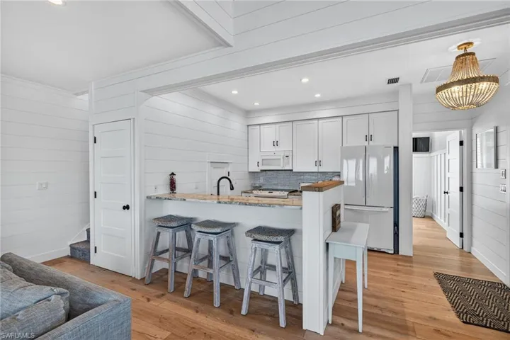 Kitchen with wood walls, white cabinetry, a peninsula, recessed lighting, and a kitchen bar