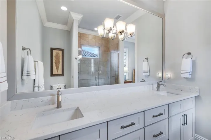 Bathroom with ornamental molding, dual vanity, toilet, and walk in shower