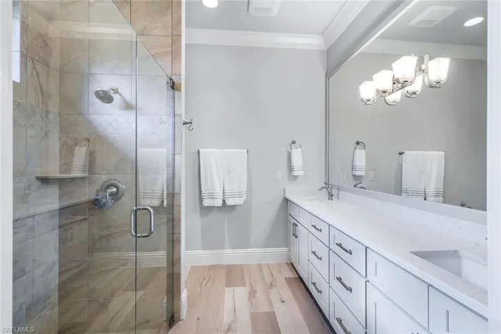 Bathroom featuring a shower with door, ornamental molding, hardwood / wood-style flooring, and dual bowl vanity