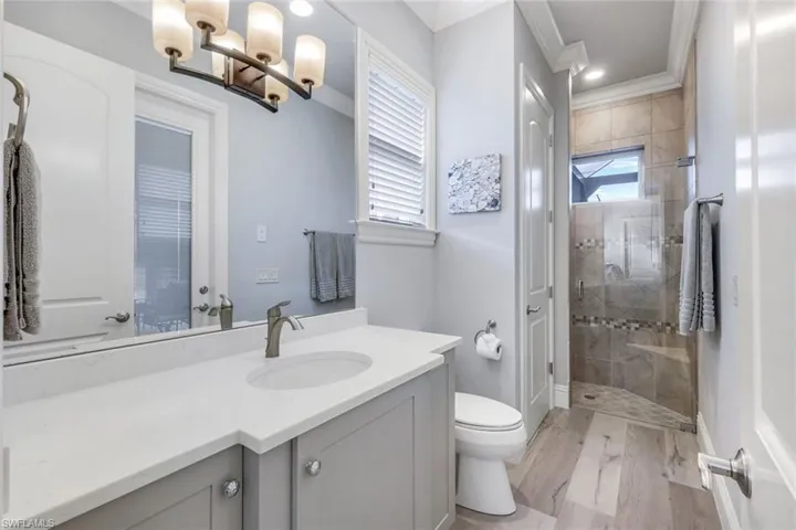 Bathroom featuring vanity, wood-type flooring, ornamental molding, a tile shower, and toilet