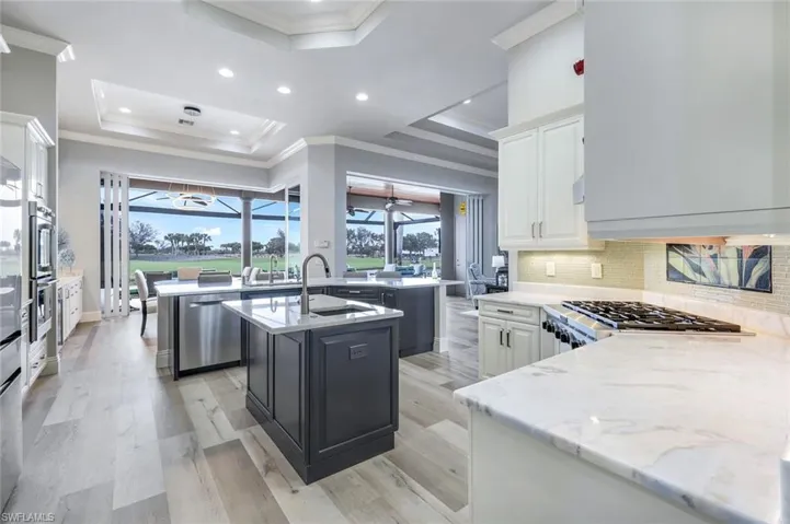 Kitchen with stainless steel appliances, a tray ceiling, light wood-type flooring, and an island with sink
