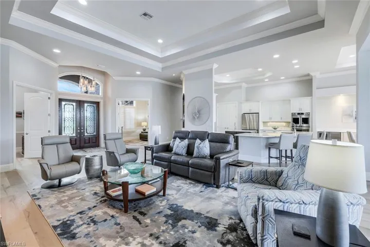 Living room with a raised ceiling, french doors, light wood-type flooring, and ornamental molding