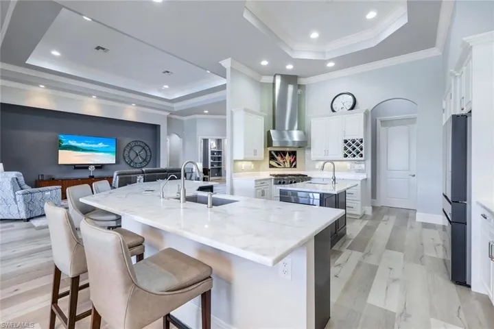 Kitchen with wall chimney exhaust hood, sink, a breakfast bar area, a raised ceiling, and a spacious island
