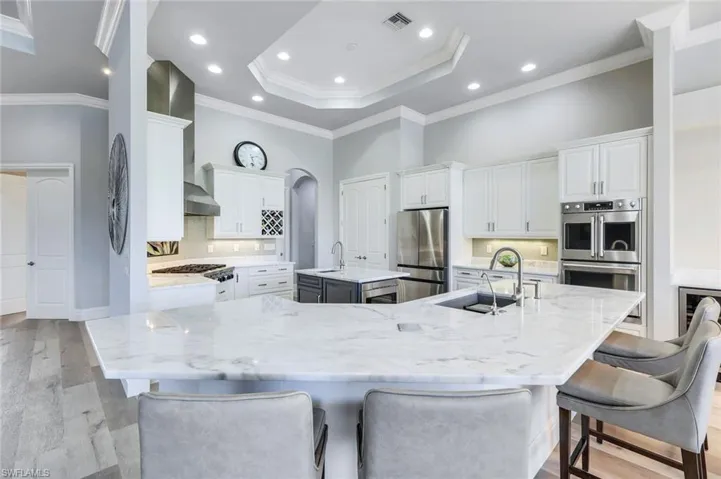Kitchen with light hardwood / wood-style flooring, decorative backsplash, white cabinetry, a tray ceiling, and a spacious island