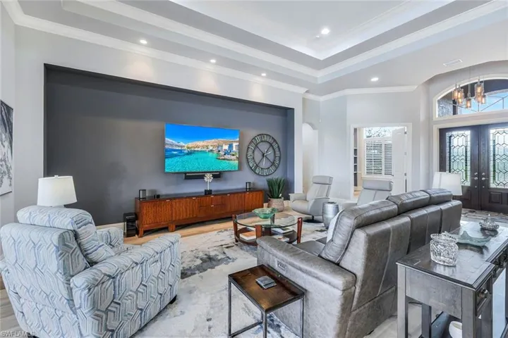 Living room with hardwood / wood-style flooring, a tray ceiling, a chandelier, ornamental molding, and french doors