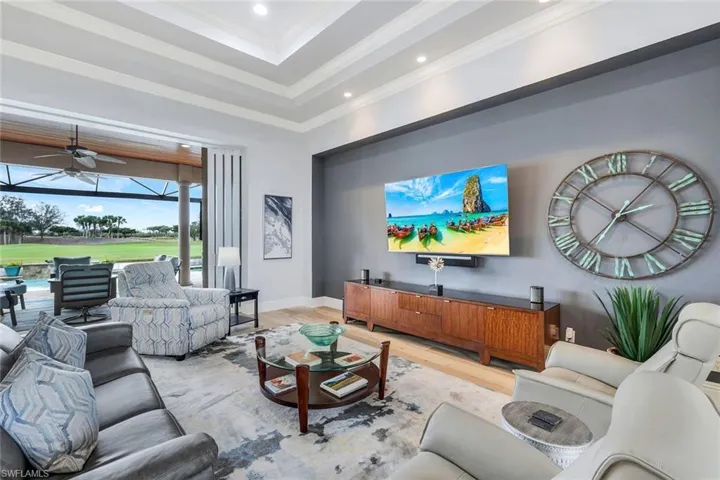Living room with a tray ceiling, light wood-type flooring, ceiling fan, and ornamental molding