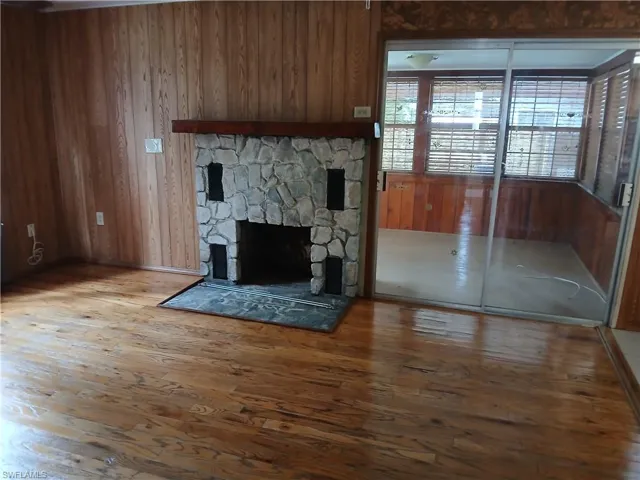 Living room with a stone fireplace, wood flooring and entry to enclosed porch